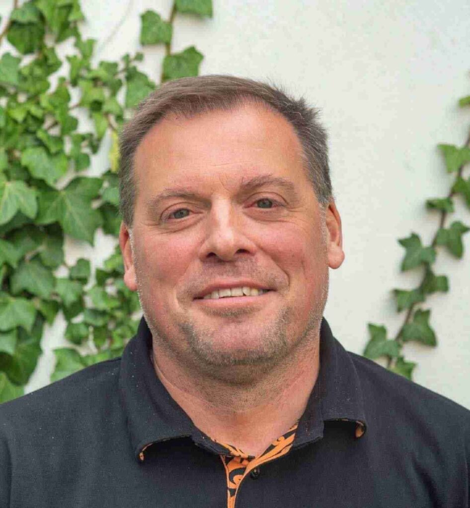 Portrait de David Vander Biest, consultant en stratégie et communication pour les ONG et ASBL, souriant devant un mur recouvert de lierre.